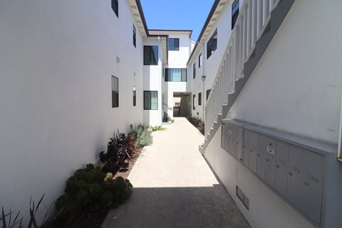 an alley between two white buildings with balconies and plants