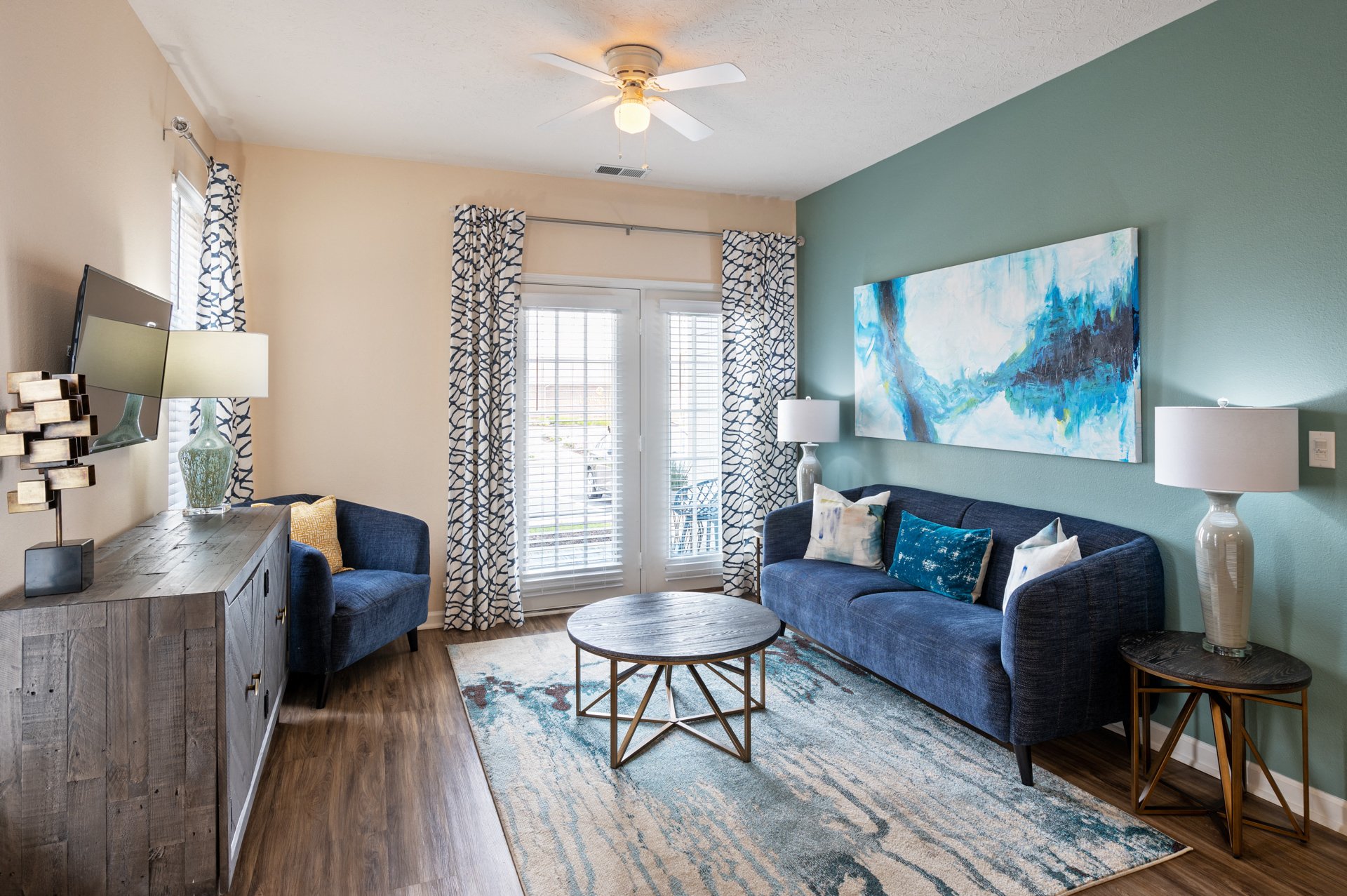 A living room with a blue couch and a painting on the wall.