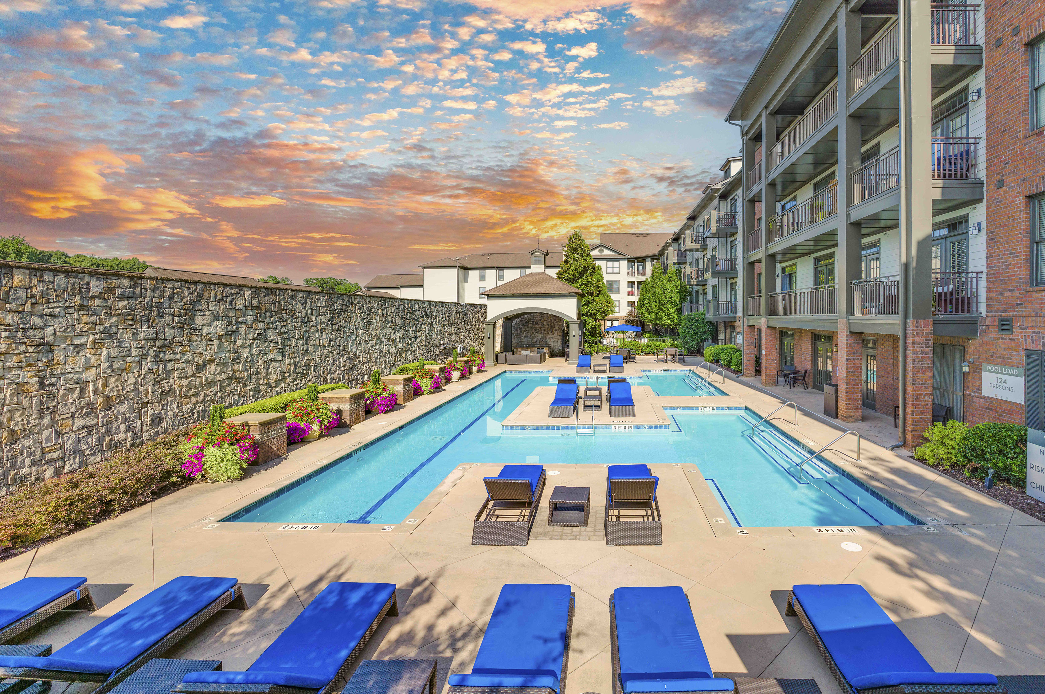 an outdoor pool with blue lounge chairs and an apartment building