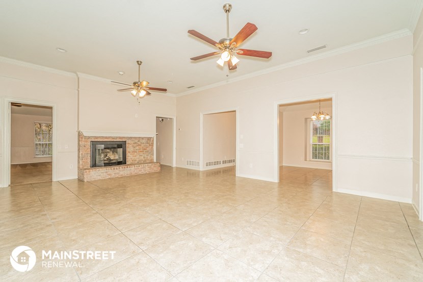 an empty living room with a fireplace and two ceiling fans