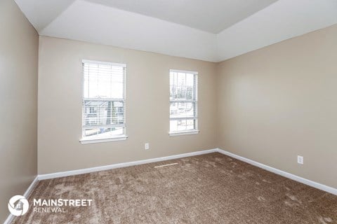 the living room of a new home with carpet and two windows