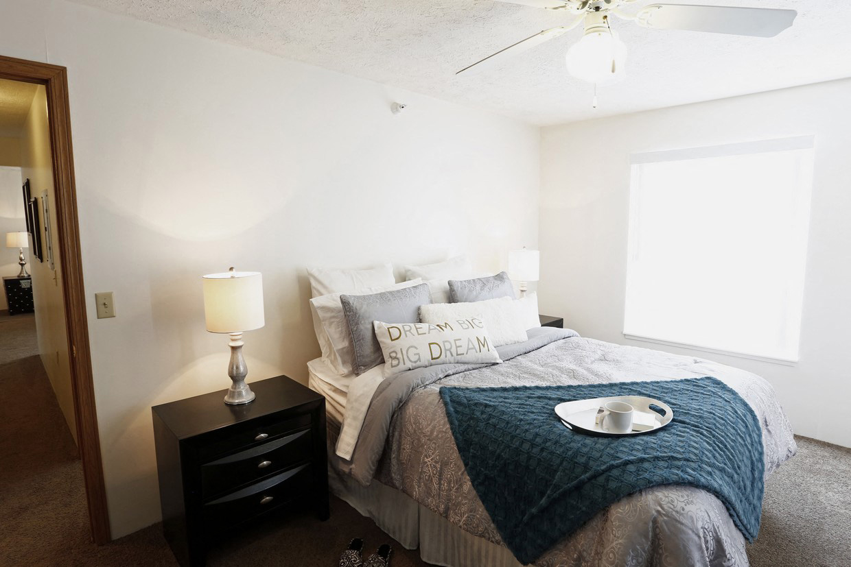 A bedroom with a bed, a nightstand with a lamp, and a ceiling fan.