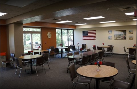 A room with tables and chairs and an American flag on the wall.