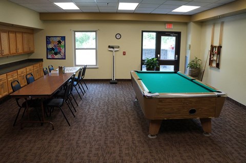 A room with a pool table and chairs.