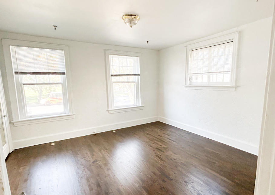 an empty room with wood floors and two windows