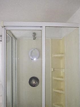 a shower with a glass door and a reflection of a shelf in it