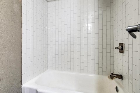 a white tiled bathroom with a tub and a sink