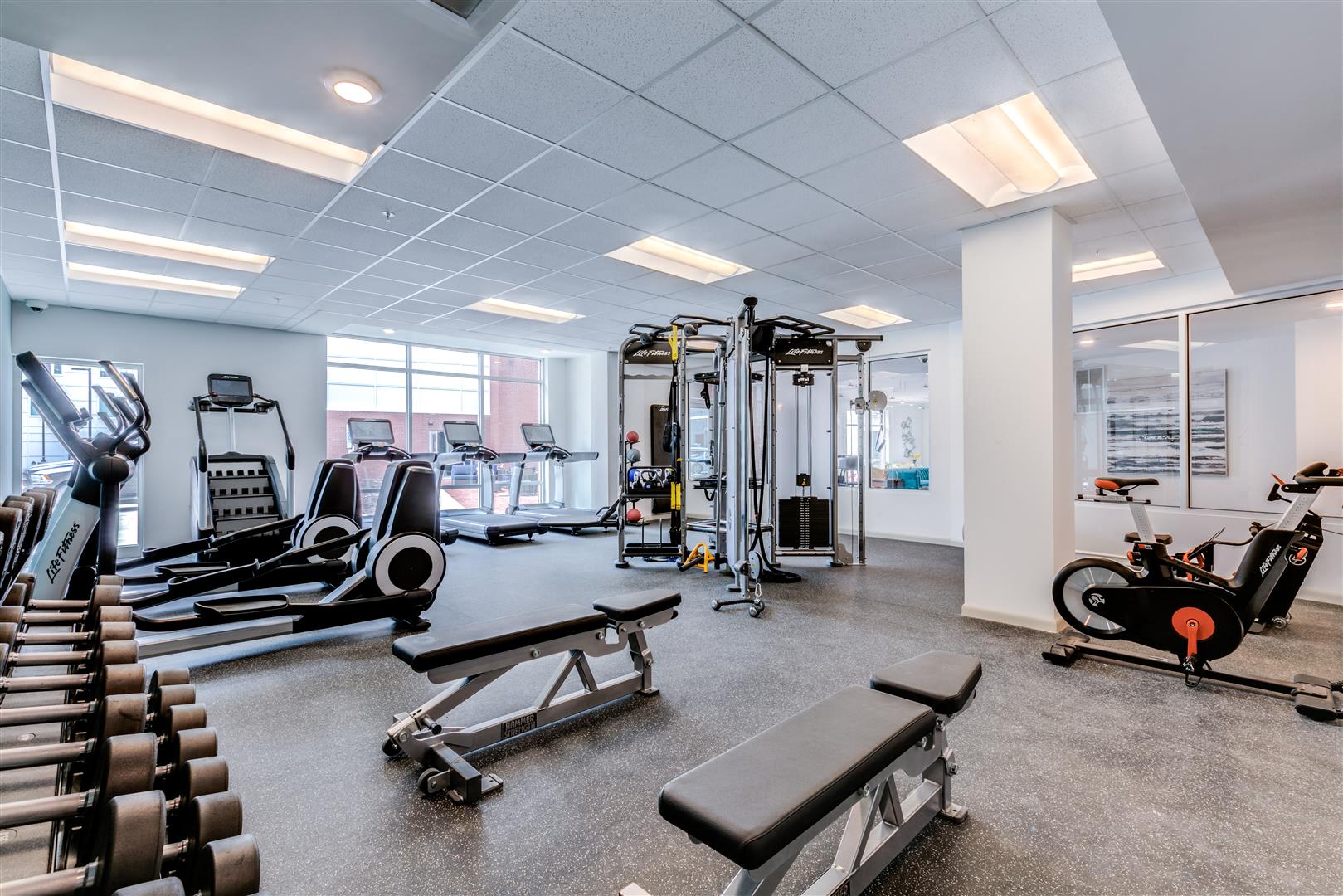 a gym with cardio equipment and weights in a building with windows