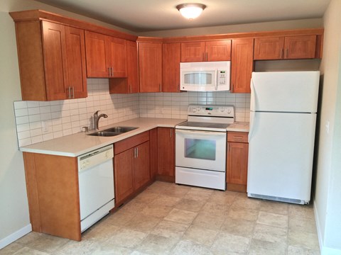 an empty kitchen with white appliances and wooden cabinets