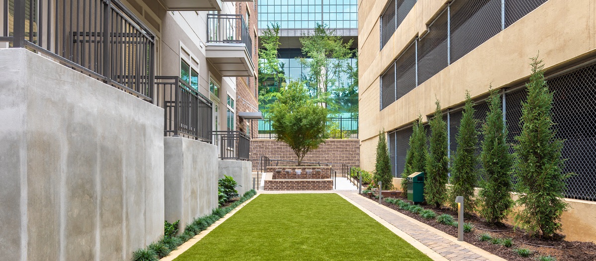 a courtyard between two buildings with green grass and a staircase