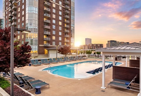 A large swimming pool surrounded by lounge chairs and umbrellas in front of a modern apartment building.