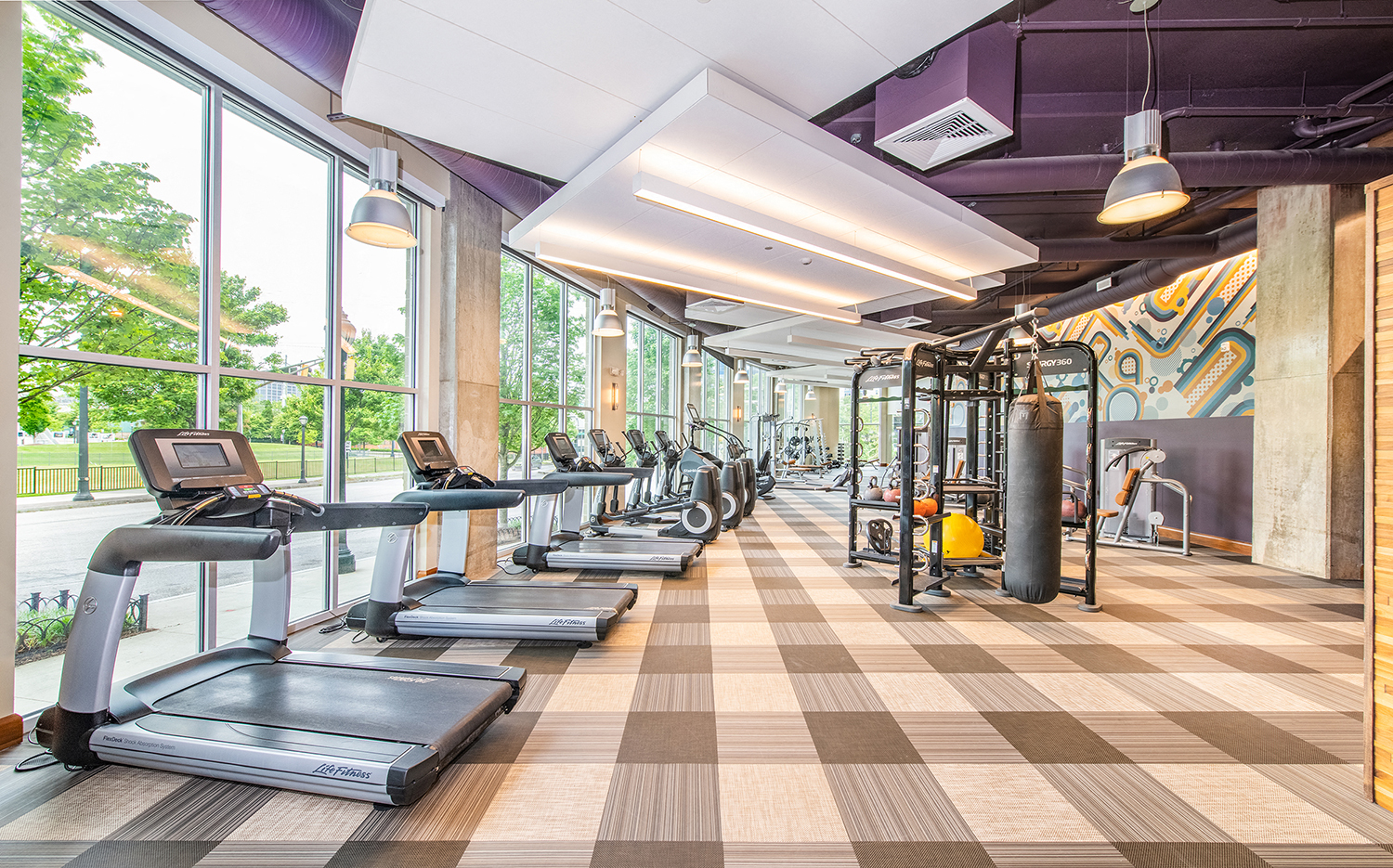 a gym with cardio equipment and large windows
