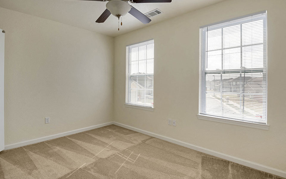 an empty bedroom with a ceiling fan and two windows