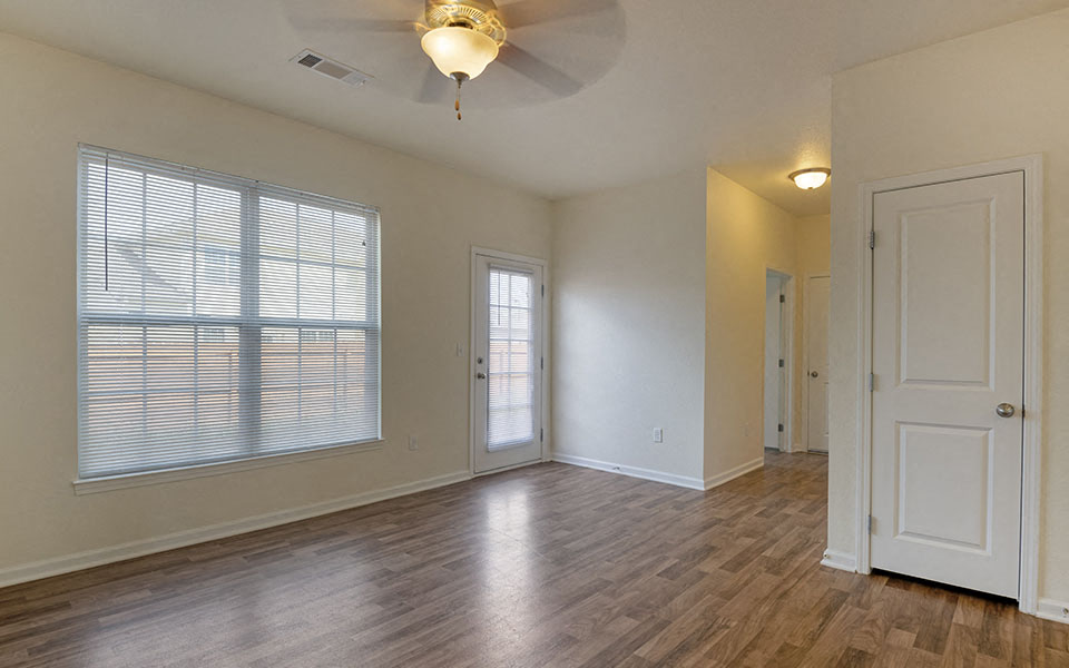 an empty living room with a large window and a ceiling fan