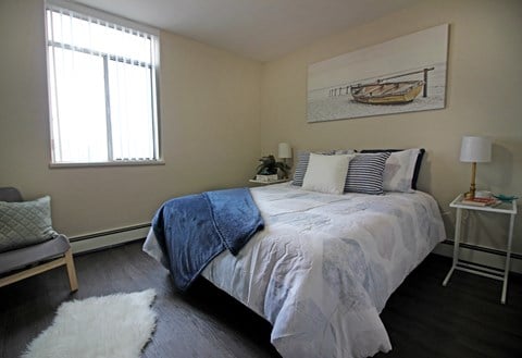 A bedroom with a bed, a chair, a lamp, and a painting on the wall.