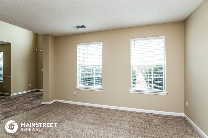 an empty living room with two windows and a carpet