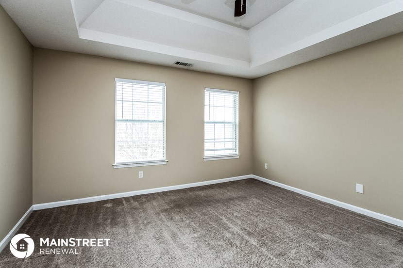 the spacious living room of a new home with carpet and two windows