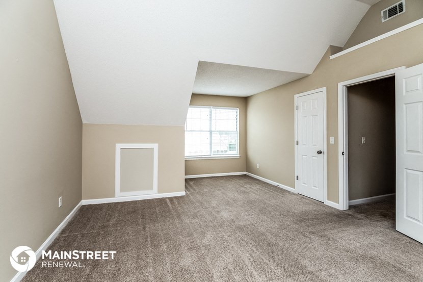 the living room of an apartment with carpeted flooring and a window