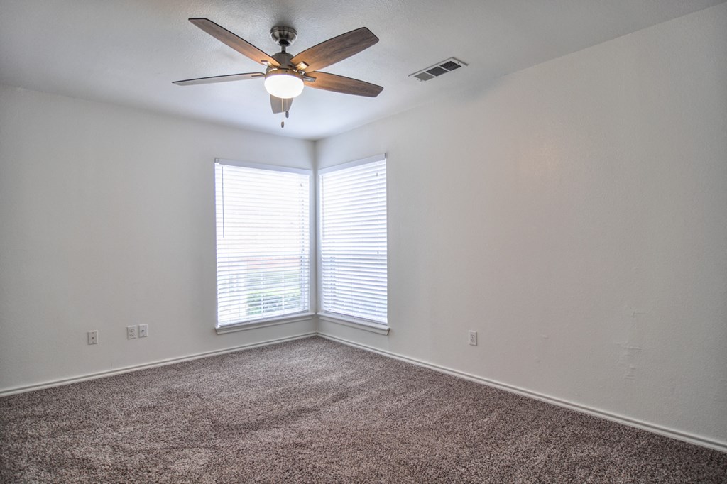 an empty room with a ceiling fan and two windows