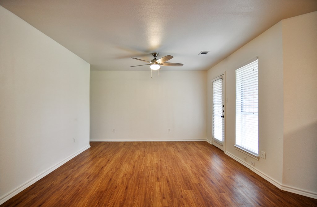 an empty living room with wood floors and a ceiling fan