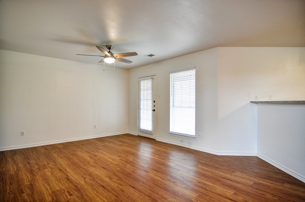 an empty living room with wood floors and a ceiling fan