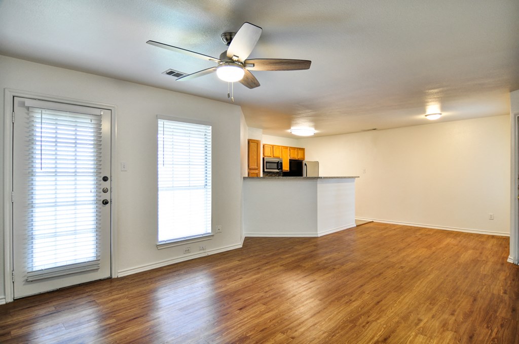 an empty living room with a ceiling fan and a kitchen
