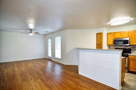 an empty living room with a kitchen and a ceiling fan