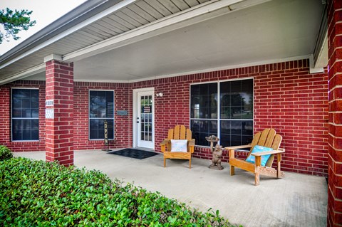 a covered porch with two chairs in front of a brick house
