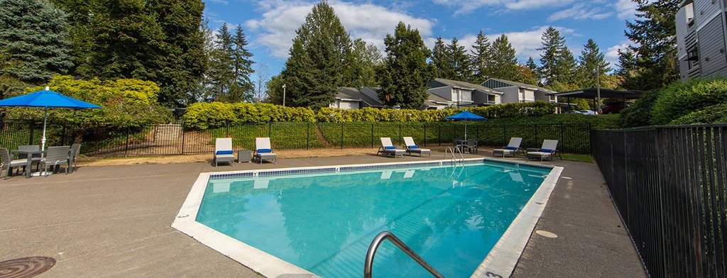 a swimming pool with chairs and umbrellas in front of a house