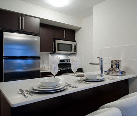 A kitchen with a stainless steel refrigerator, microwave, and white countertop.
