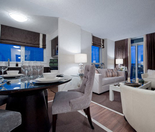 A modern dining room with a table set for two and a couch in the background.