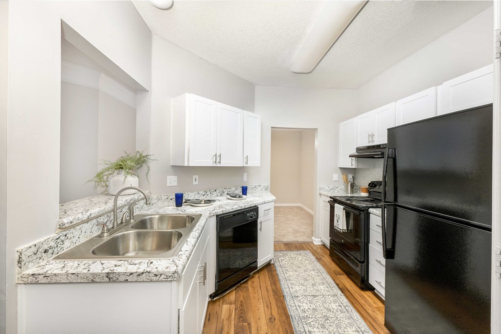 A kitchen with a black refrigerator, white cabinets, and a marble countertop.