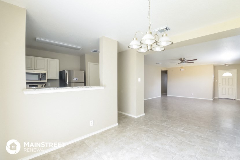 an empty living room with a kitchen and a ceiling fan