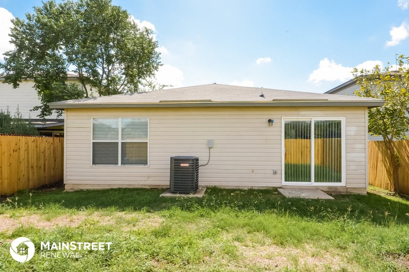 the backyard of a small white house with a yard and a fence