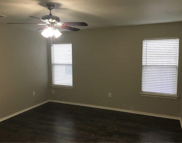 an empty room with a ceiling fan and two windows