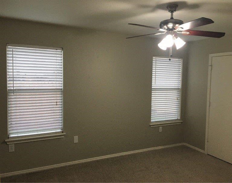 an empty room with a ceiling fan and two windows