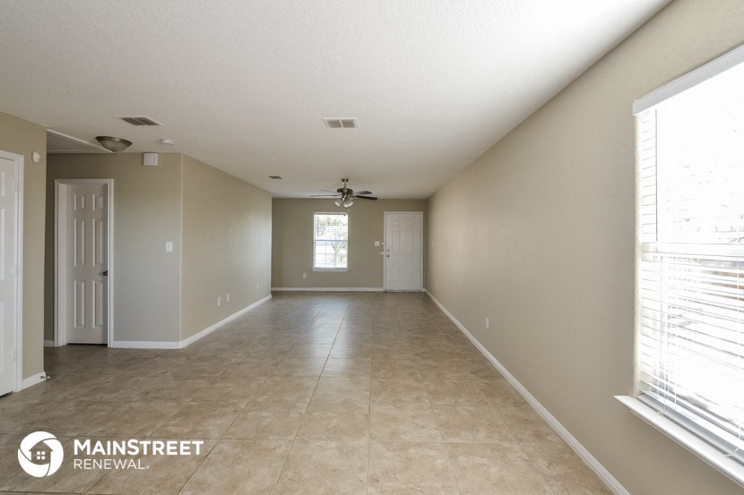 an empty living room with beige tile and a window