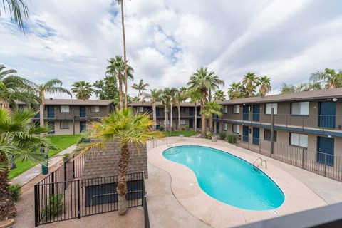 a resort style swimming pool in front of a building with palm trees