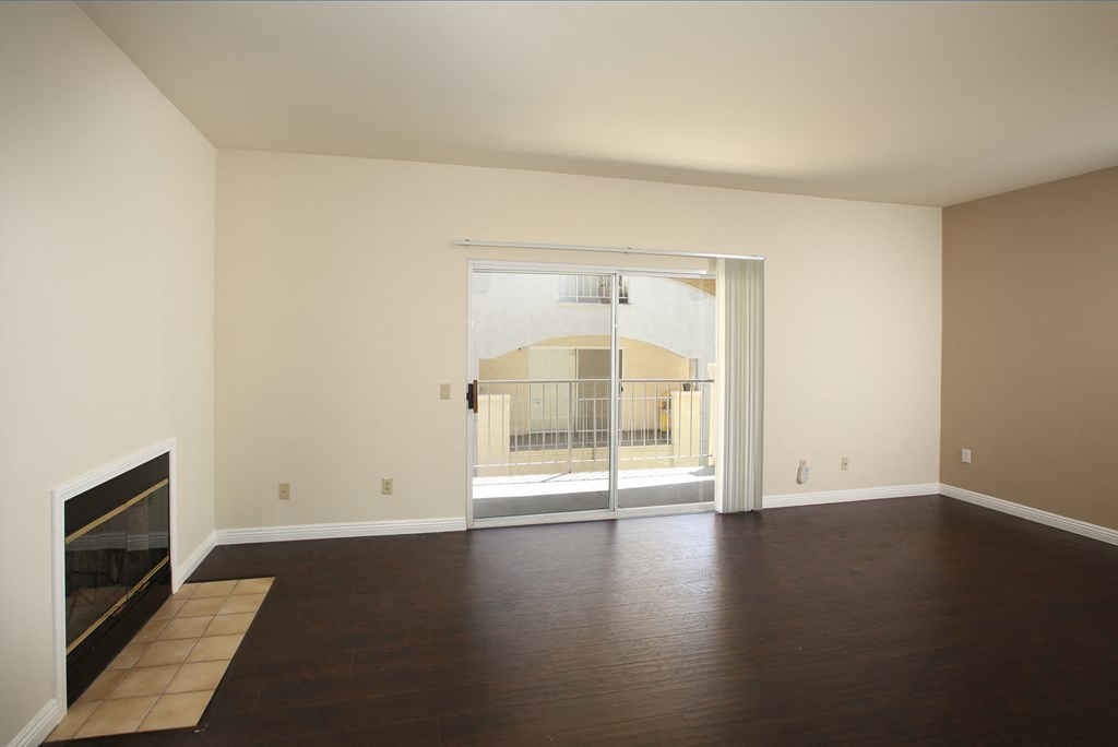 an empty living room with a fireplace and a sliding glass door to a balcony