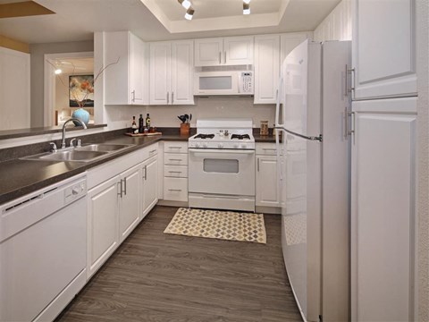 A kitchen with white cabinets and appliances, a sink, and a rug on the floor.