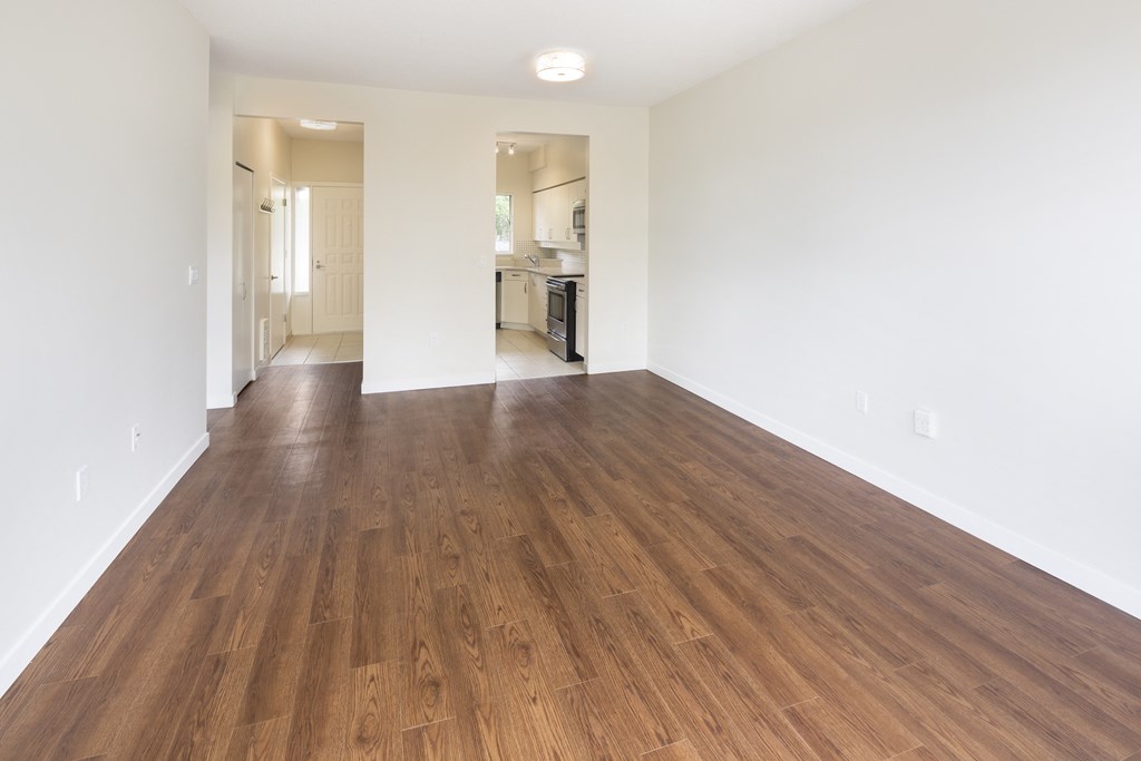 an empty living room with wood flooring and a kitchen