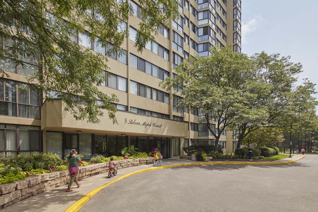 people walking in front of a tall building with a street in front
