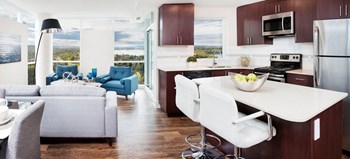 Kitchen and dining area with brown cupboards, white countertops, light brown vinyl plank flooring and a white dining set. - Photo Gallery 2