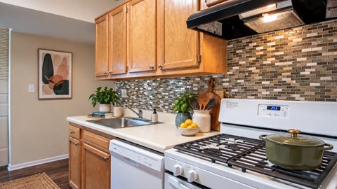 A kitchen with a white stove top oven and wooden cabinets.