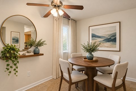 A dining room with a round table and chairs, a ceiling fan, and a painting on the wall.