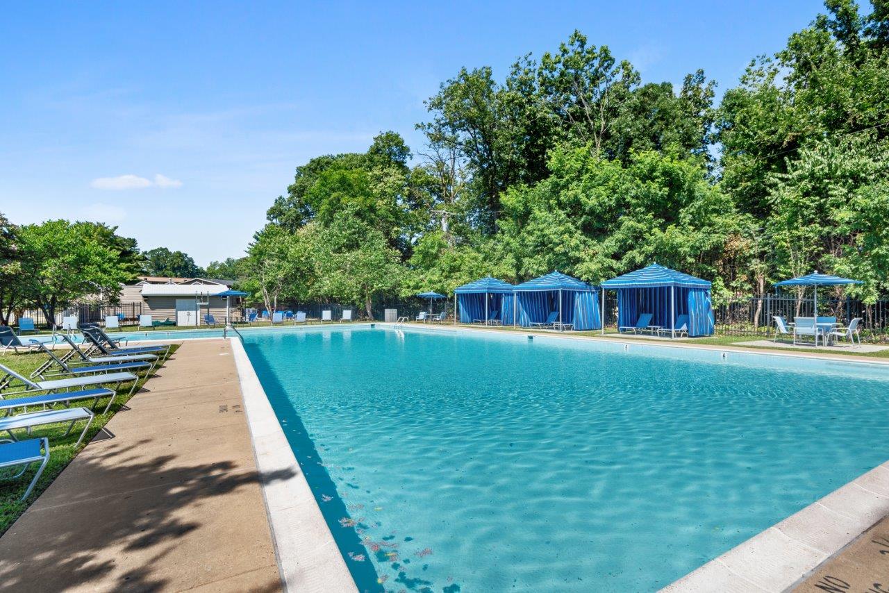 a large pool with chairs and blue umbrellas near some trees