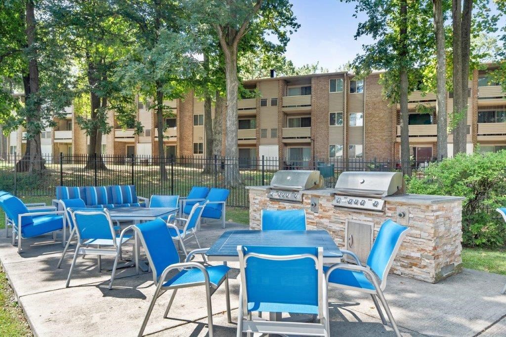 a patio with tables and chairs and a grill in front of an apartment building