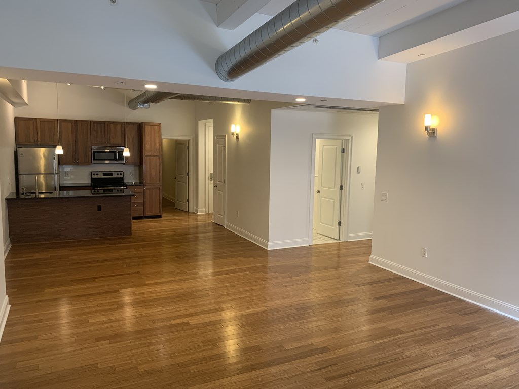 an empty living room with wood floors and a kitchen