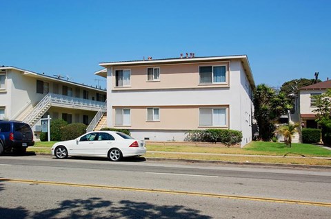 A white car is parked on the side of the road in front of a two-story building.
