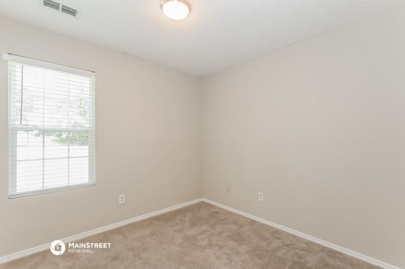 a bedroom with a window and beige carpet and white walls